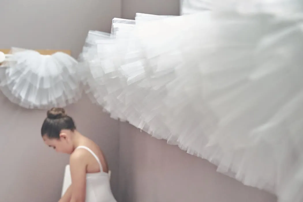 Coulisses — Tutus suspendus au-dessus d'une jeune danseuse.