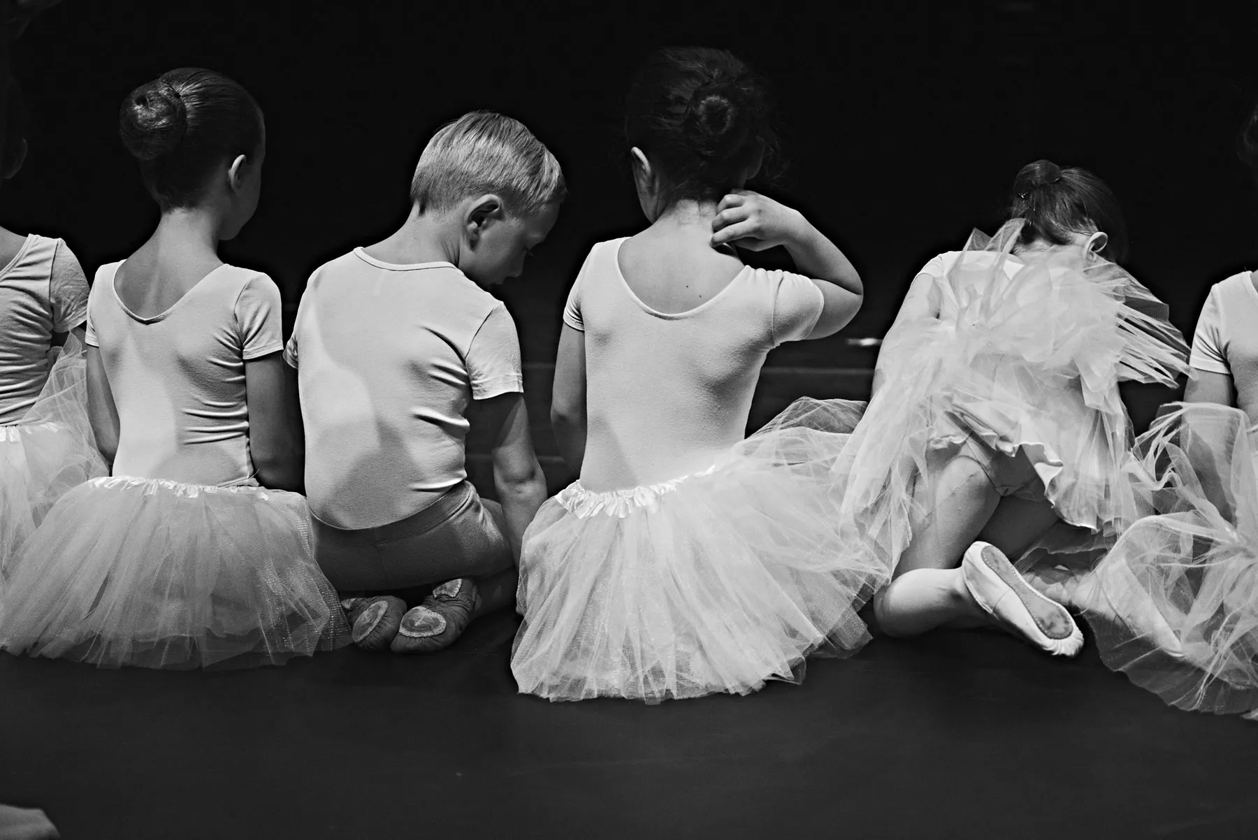 De jeunes danseurs en tutu assis de dos en coulisses, avant l'entrée en scène.
