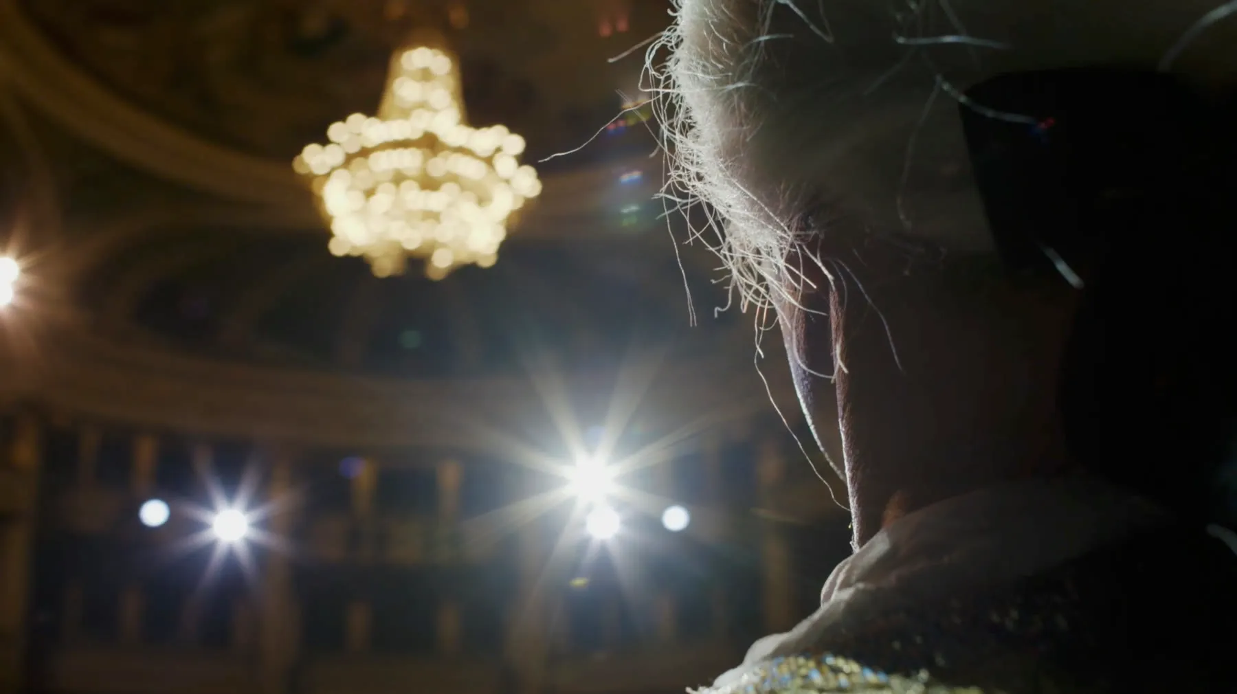 Salle de l'Opéra National de Bordeaux vue de scène, lustre allumé et coiffe d'artiste au premier plan.